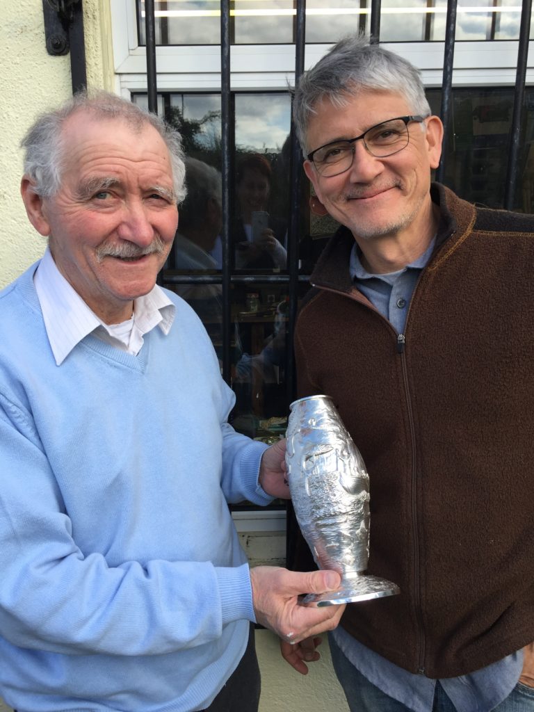 Two men holding a trophy in front of a building.