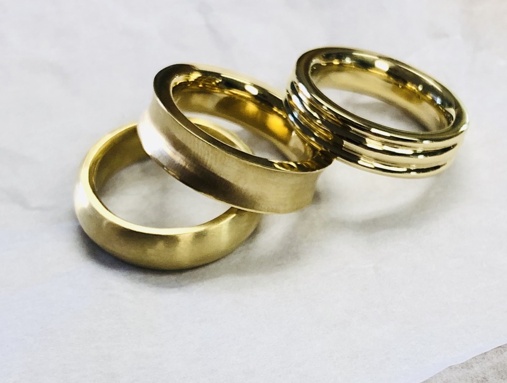 Three gold rings are sitting on a white surface.