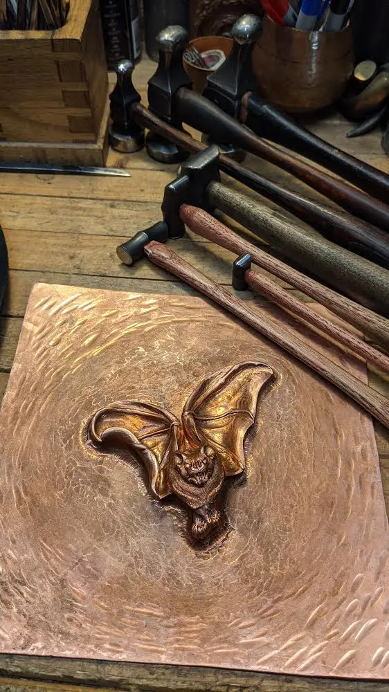 A bat carved into wood with hammers in the background.
